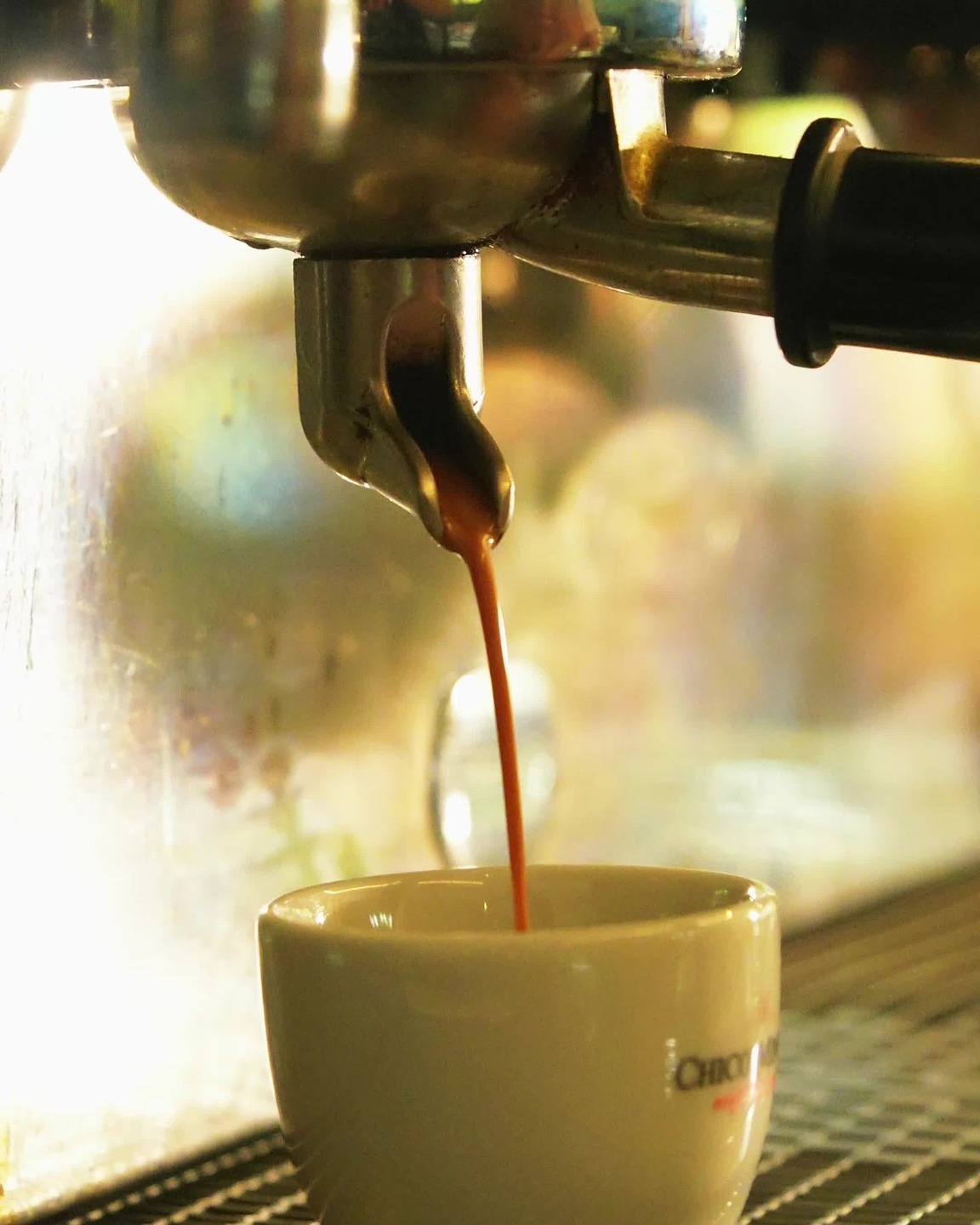 Extração de espresso caindo em xícara branca da casa, com contraluz sobre a máquina