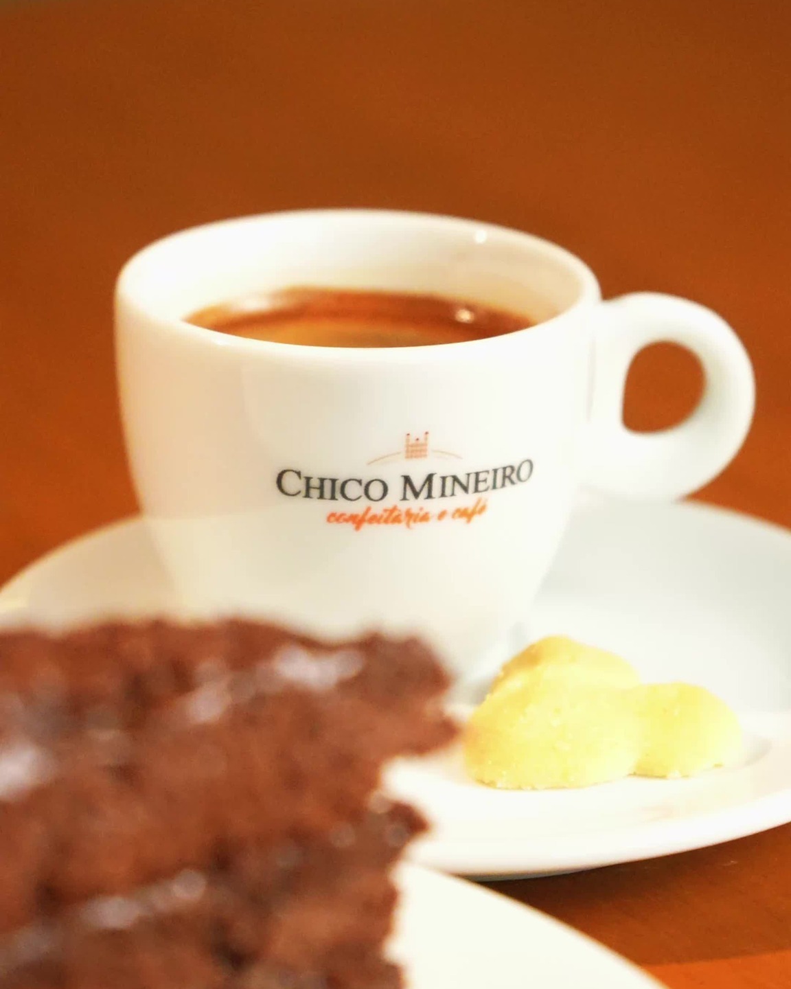 Xícara de café da Chico Mineiro Confeitaria com fatia de bolo de chocolate e broinhas de fubá